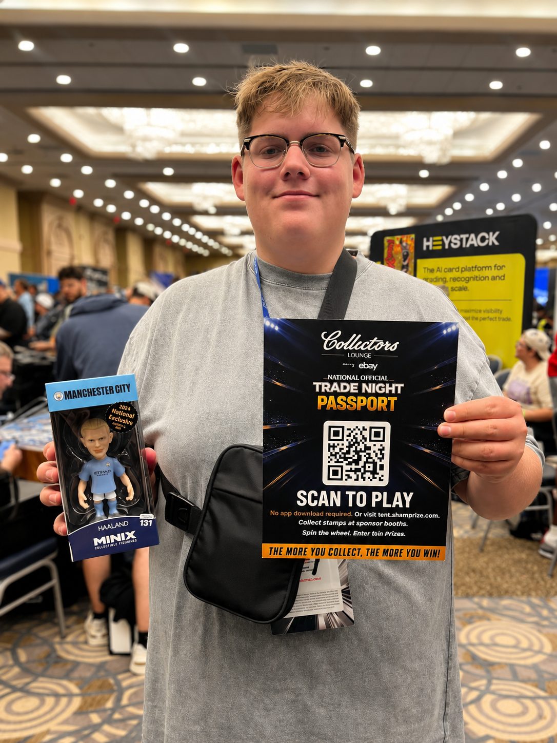 A collector holding the Scan to Play Trade Night Passport poster and a Minix prize